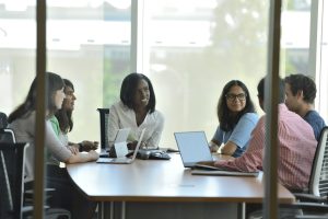 Students with laptops meet in a conference room.